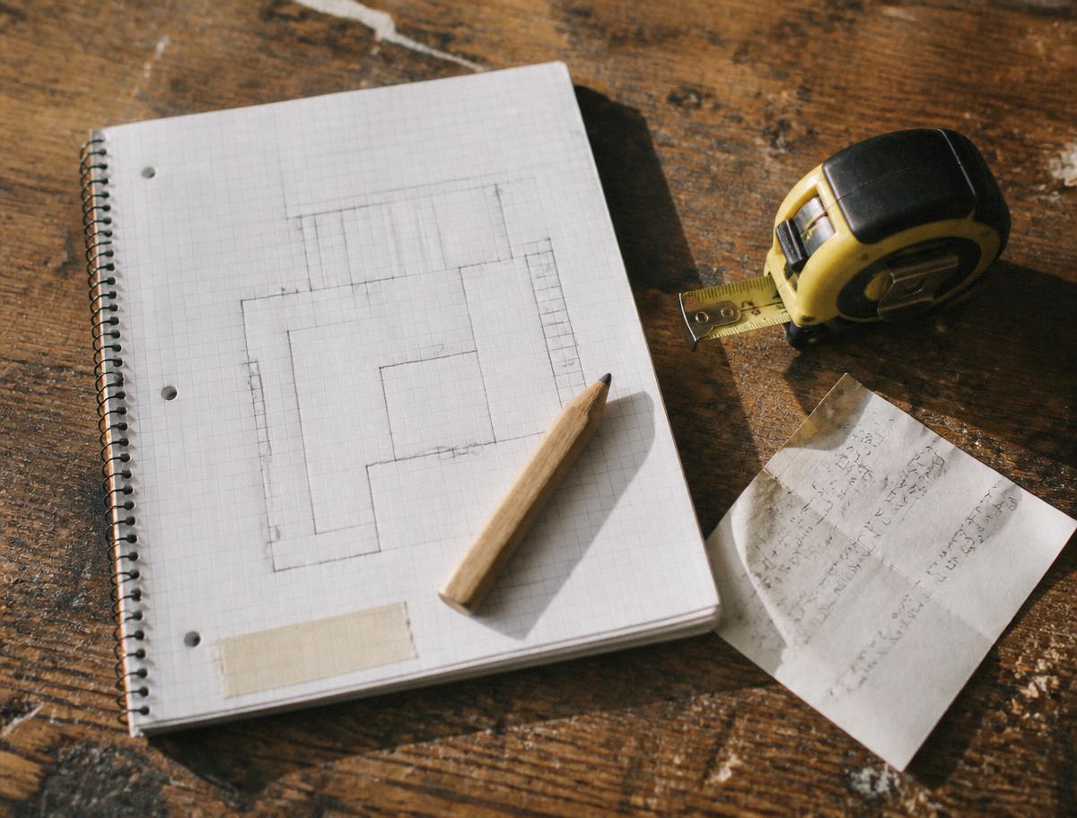 A graph-paper notebook with a hand-sketched shop layout, a carpenter pencil, tape measure, and a receipt with handwritten math